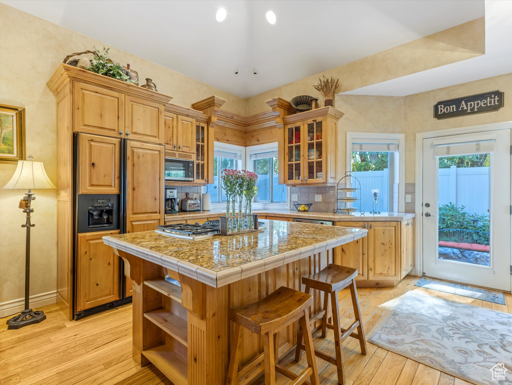 Kitchen featuring built in appliances, a center island, light wood-style flooring, glass insert cabinets, and tasteful backsplash