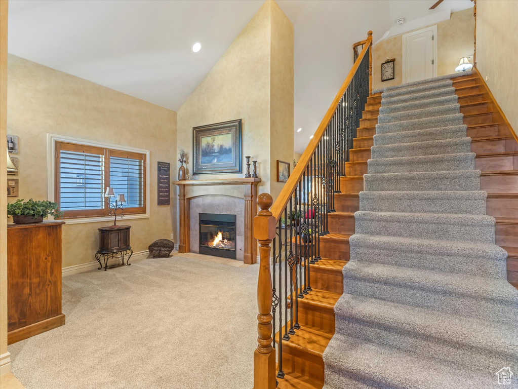 Stairway with a glass covered fireplace, high vaulted ceiling, and carpet floors