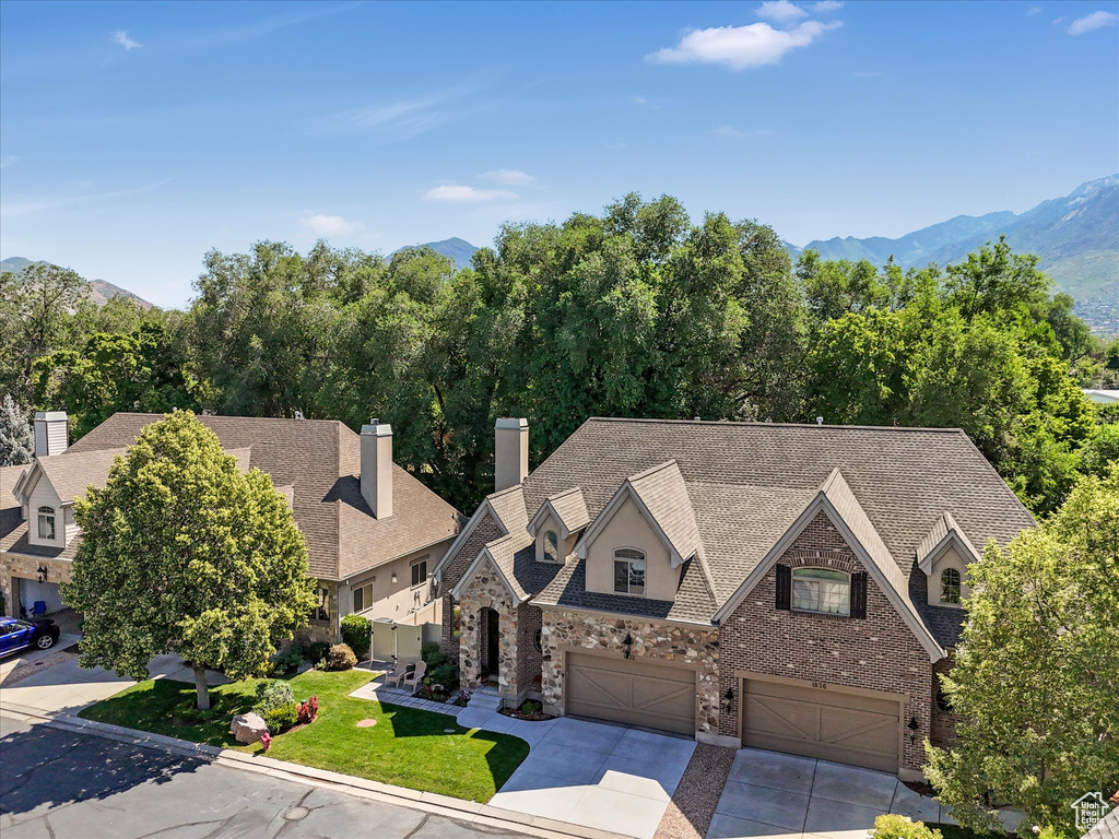 View of front of property featuring an attached garage, concrete driveway, a chimney, a mountain view, and roof with shingles