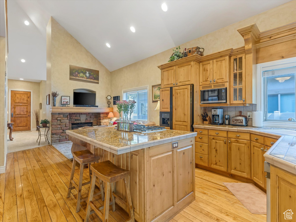 Kitchen with paneled built in refrigerator, black microwave, light wood-type flooring, a center island, and high vaulted ceiling