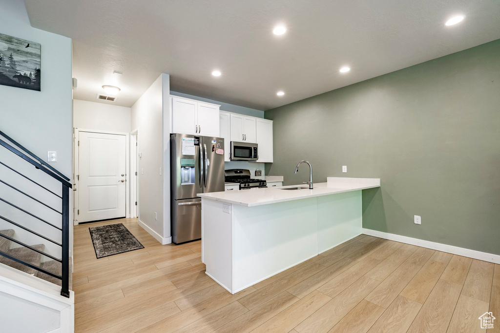 Kitchen featuring appliances with stainless steel finishes, a peninsula, light wood-style flooring, white cabinets, and light countertops
