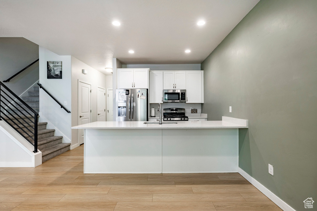 Kitchen with stainless steel appliances, a peninsula, white cabinetry, light wood-style floors, and light countertops