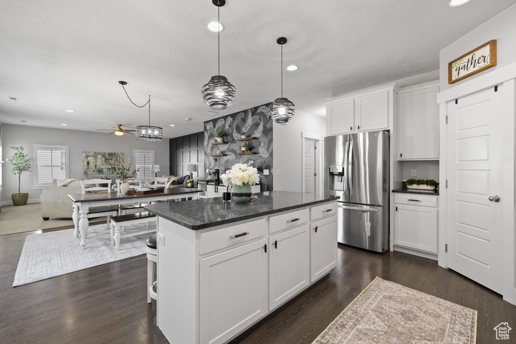 Kitchen with stainless steel fridge with ice dispenser, ceiling fan, a kitchen island, open floor plan, and white cabinetry