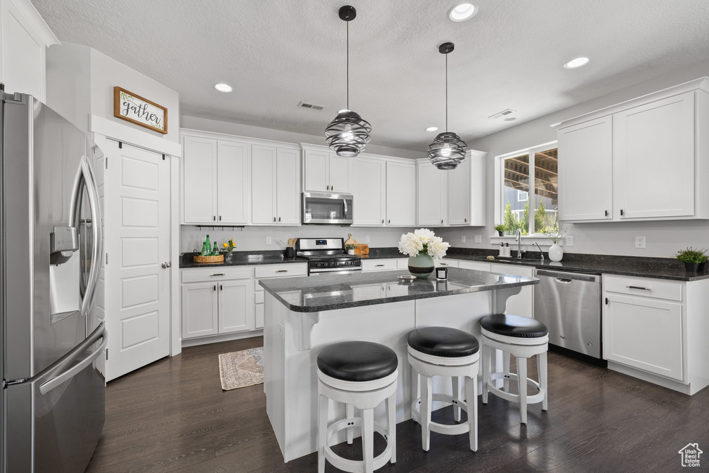 Kitchen with stainless steel appliances, recessed lighting, dark wood-style floors, white cabinetry, and a kitchen island