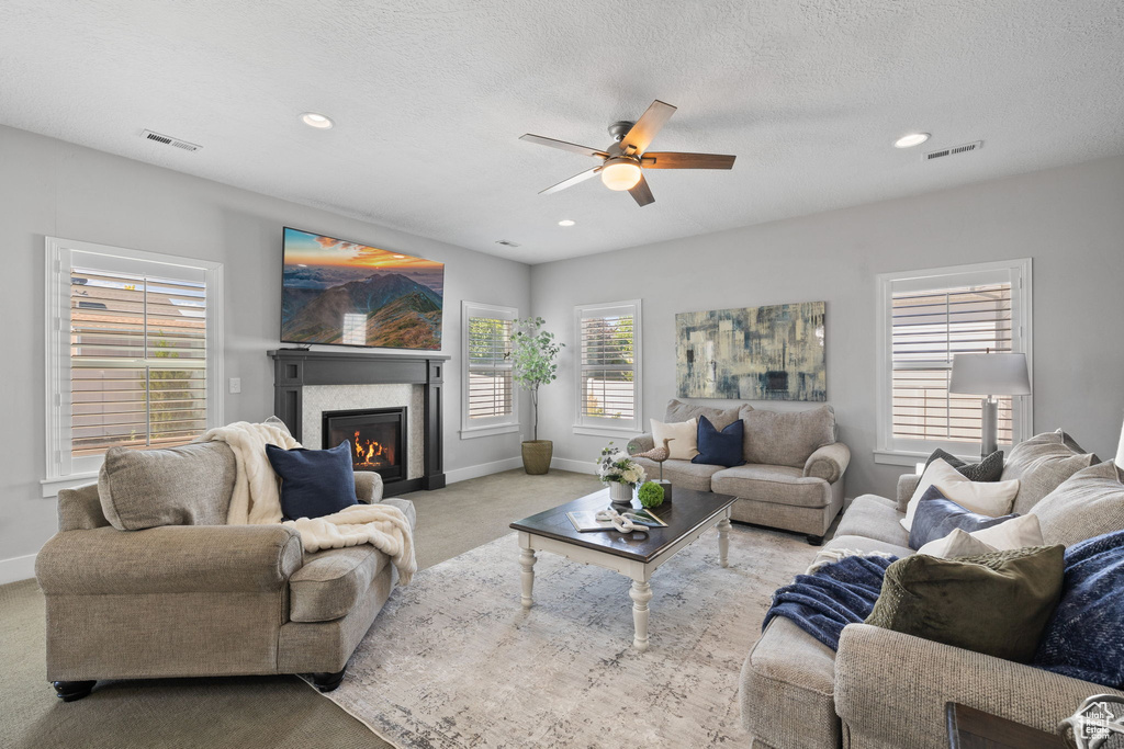 Living room with a glass covered fireplace, carpet floors, a ceiling fan, recessed lighting, and a textured ceiling