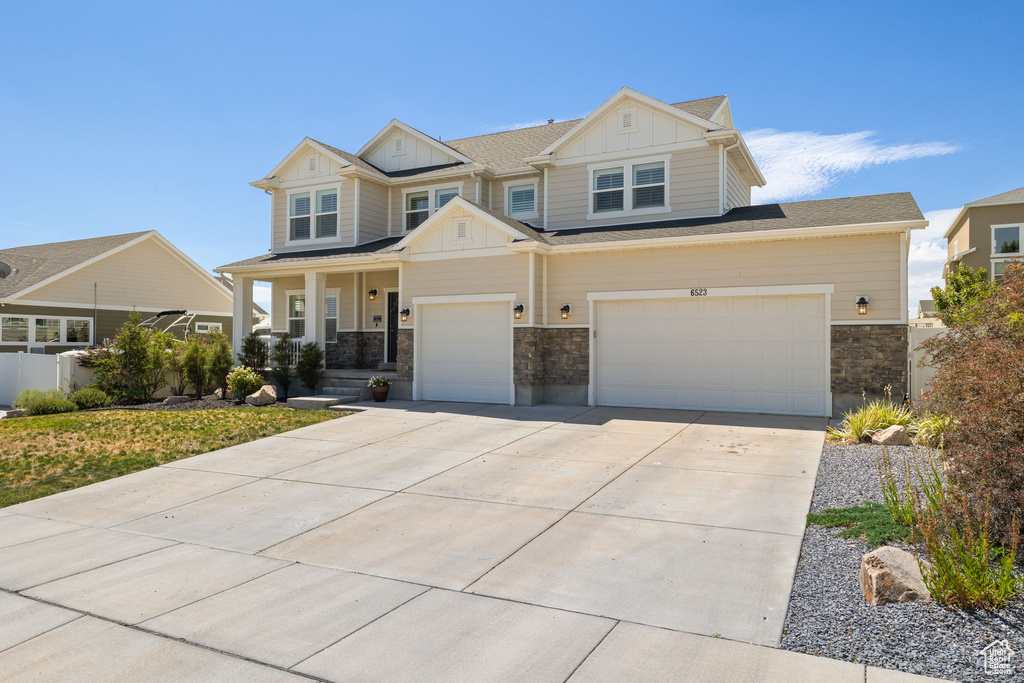Craftsman-style home with board and batten siding, concrete driveway, stone siding, a porch, and an attached garage