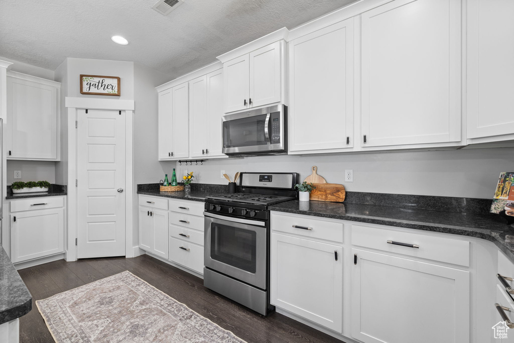 Kitchen featuring stainless steel appliances, white cabinetry, dark wood-type flooring, recessed lighting, and a textured ceiling