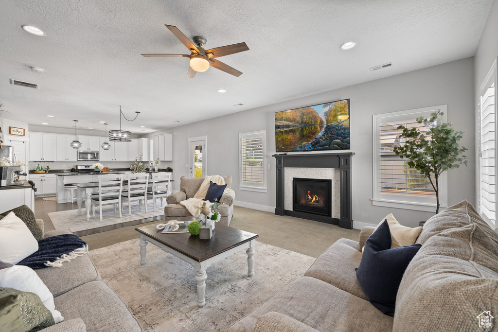 Living area featuring a ceiling fan, recessed lighting, a glass covered fireplace, healthy amount of natural light, and a textured ceiling