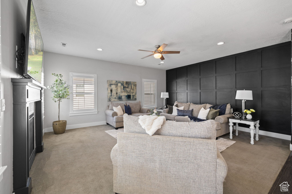 Living room with light colored carpet, recessed lighting, ceiling fan, and a decorative wall
