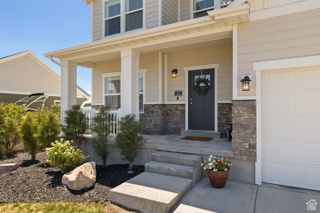 Property entrance with a garage, a porch, and stone siding