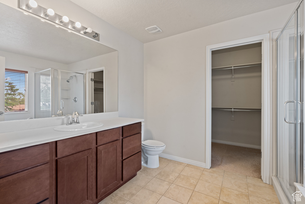 Bathroom with a walk in closet, a shower stall, vanity, tile patterned floors, and a textured ceiling
