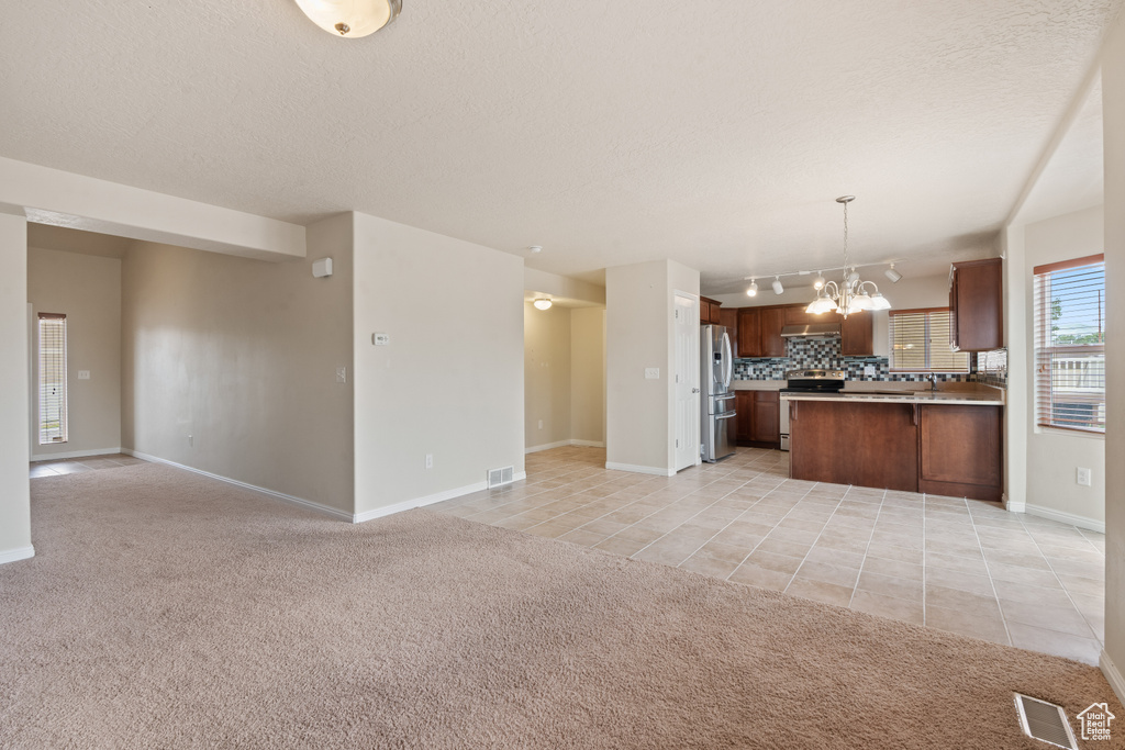 Kitchen with open floor plan, appliances with stainless steel finishes, a chandelier, light colored carpet, and a textured ceiling