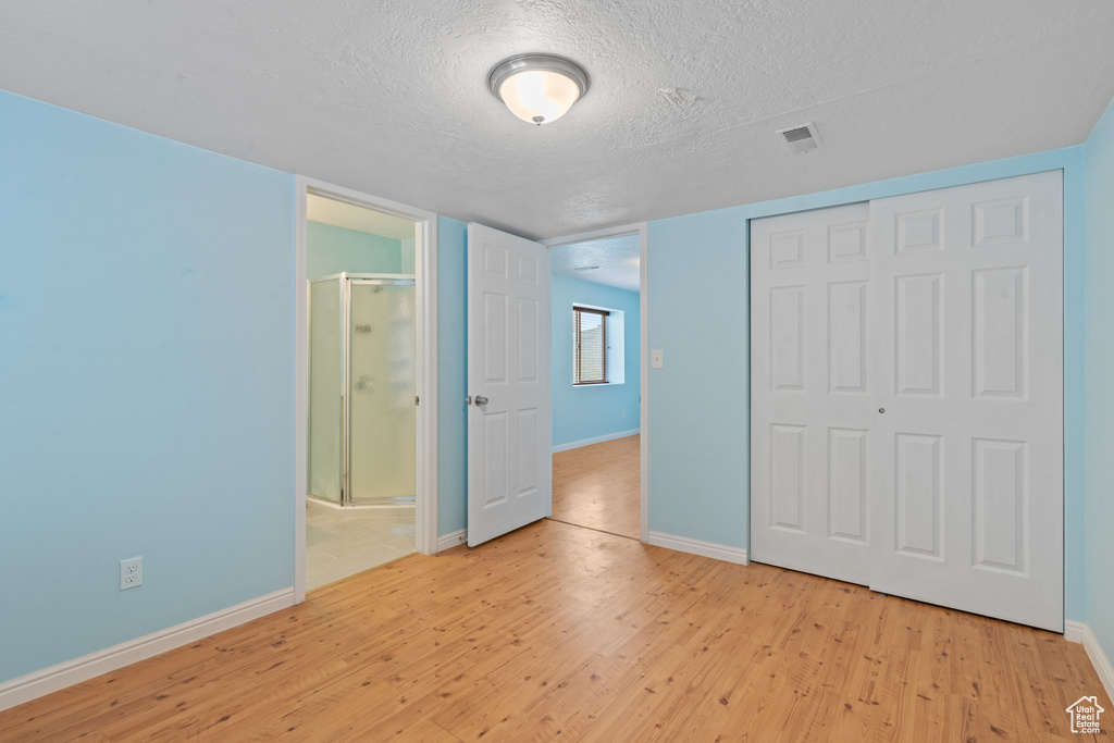 Unfurnished bedroom featuring light wood-style floors, a textured ceiling, a closet, and connected bathroom