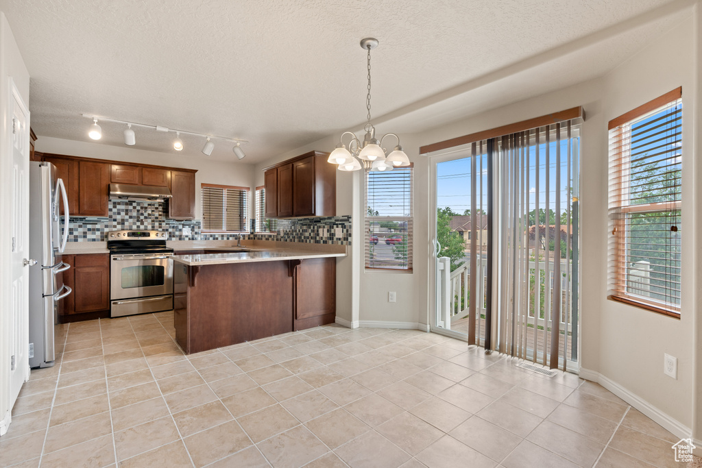 Kitchen with appliances with stainless steel finishes, under cabinet range hood, light tile patterned flooring, backsplash, and a textured ceiling