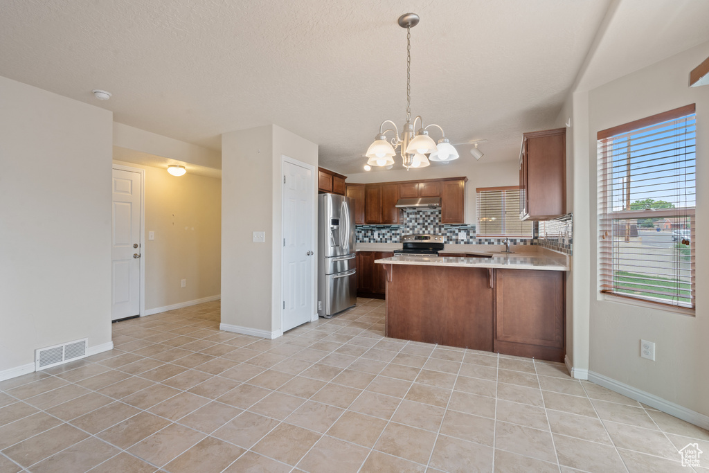 Kitchen featuring stainless steel appliances, light tile patterned flooring, tasteful backsplash, light countertops, and a chandelier