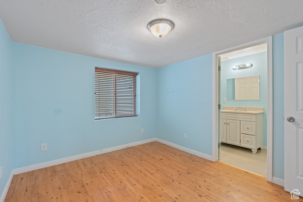 Unfurnished bedroom with light wood-type flooring, a textured ceiling, and connected bathroom