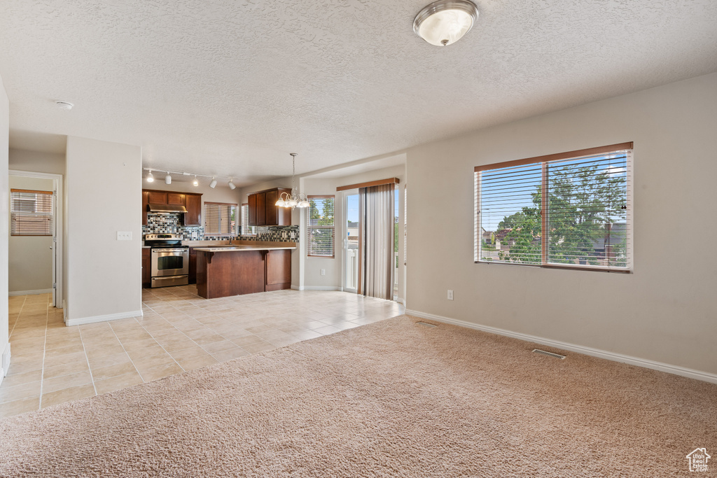 Unfurnished living room with a chandelier, light tile patterned flooring, a textured ceiling, track lighting, and light carpet