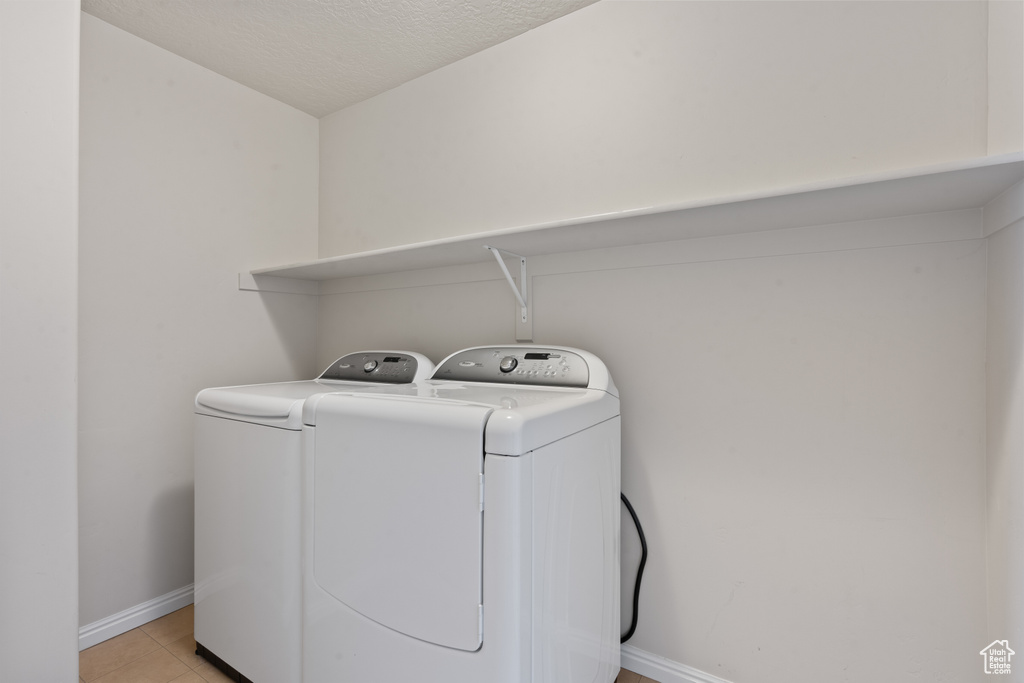 Laundry area with separate washer and dryer, a textured ceiling, and light tile patterned floors