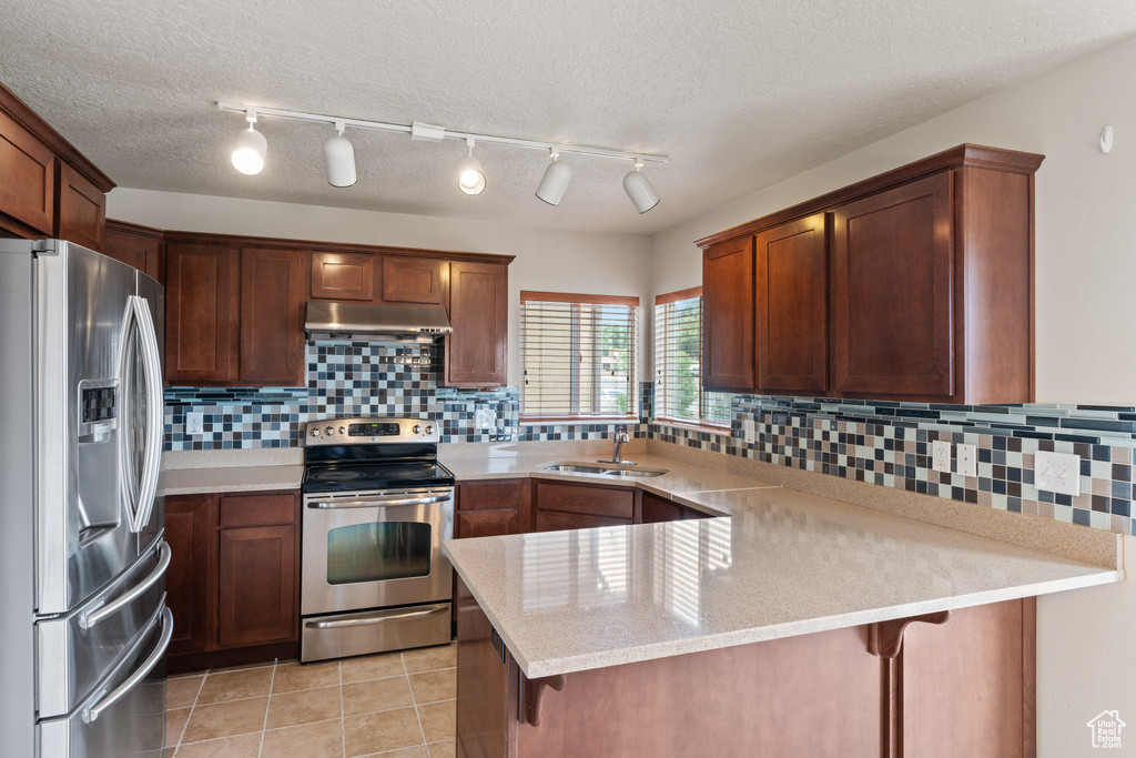 Kitchen featuring stainless steel appliances, under cabinet range hood, a peninsula, decorative backsplash, and light tile patterned floors