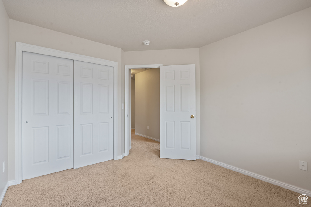 Unfurnished bedroom with light carpet and a closet
