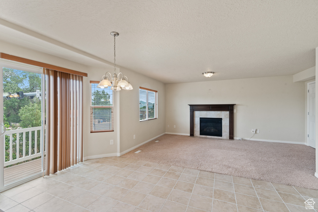 Unfurnished living room featuring a textured ceiling, light colored carpet, light tile patterned flooring, a fireplace, and a chandelier