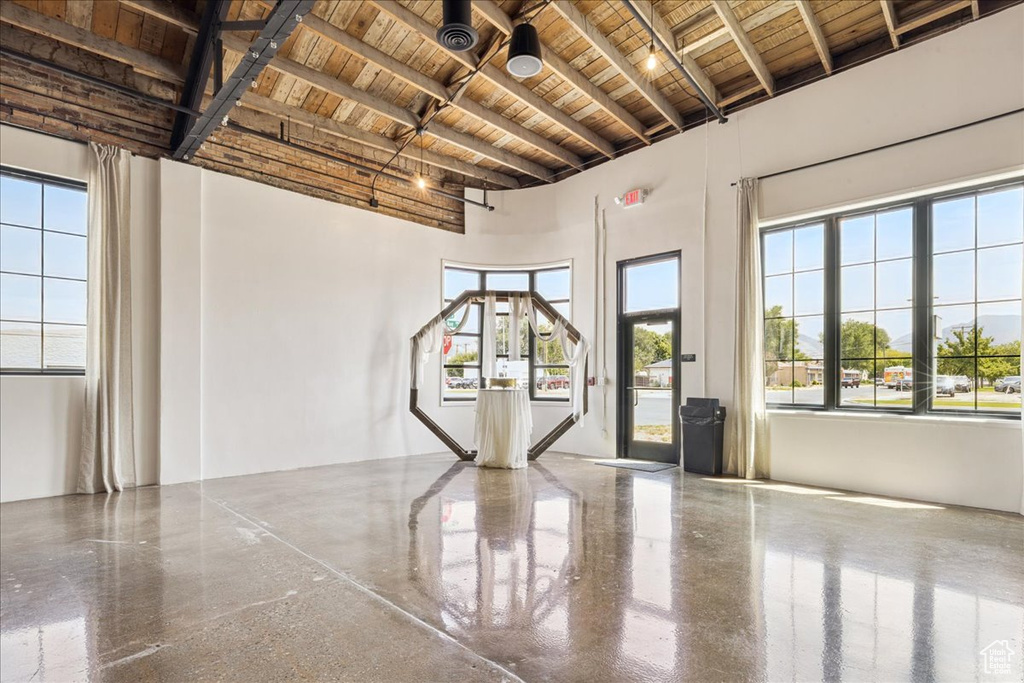Spare room featuring a wood ceiling with exposed beams, a high ceiling, and speckle patterned floor