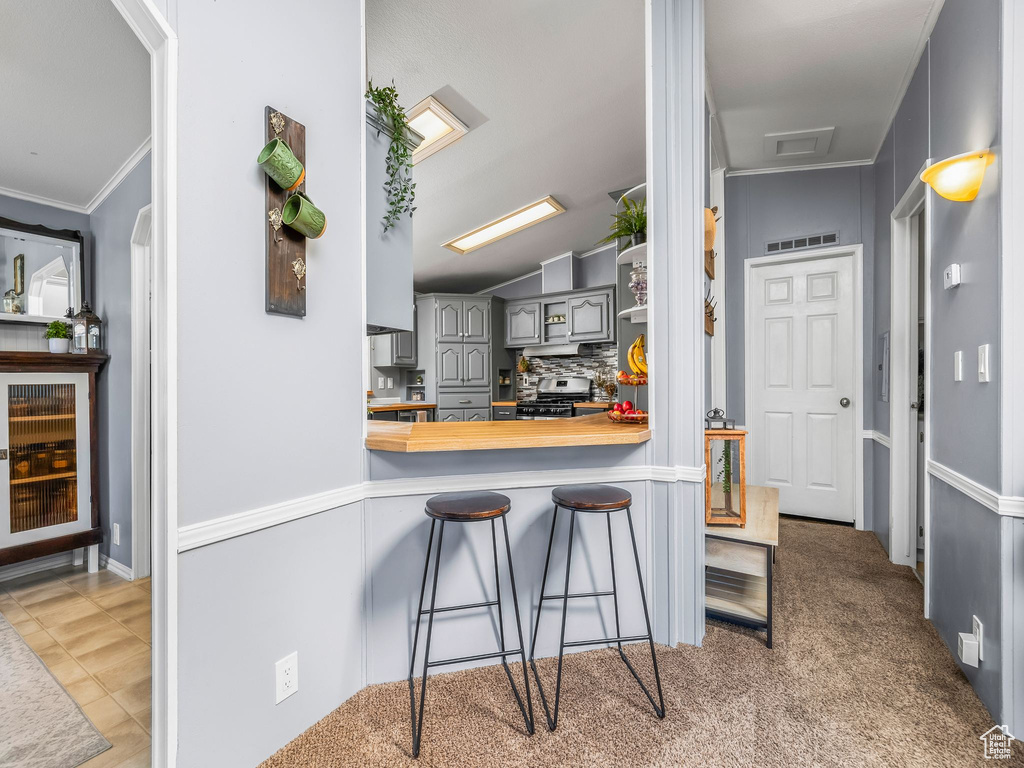 Kitchen with stainless steel gas range oven, gray cabinets, a kitchen bar, decorative backsplash, and ornamental molding