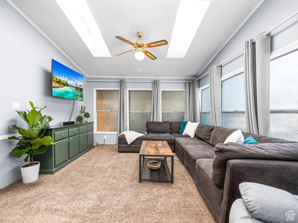 Carpeted living area with a skylight, crown molding, ceiling fan, vaulted ceiling, and plenty of natural light