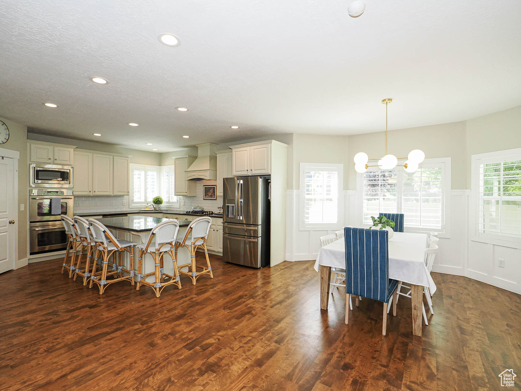 Dining area featuring a chandelier, dark wood-type flooring, a wainscoted wall, recessed lighting, and plenty of natural light