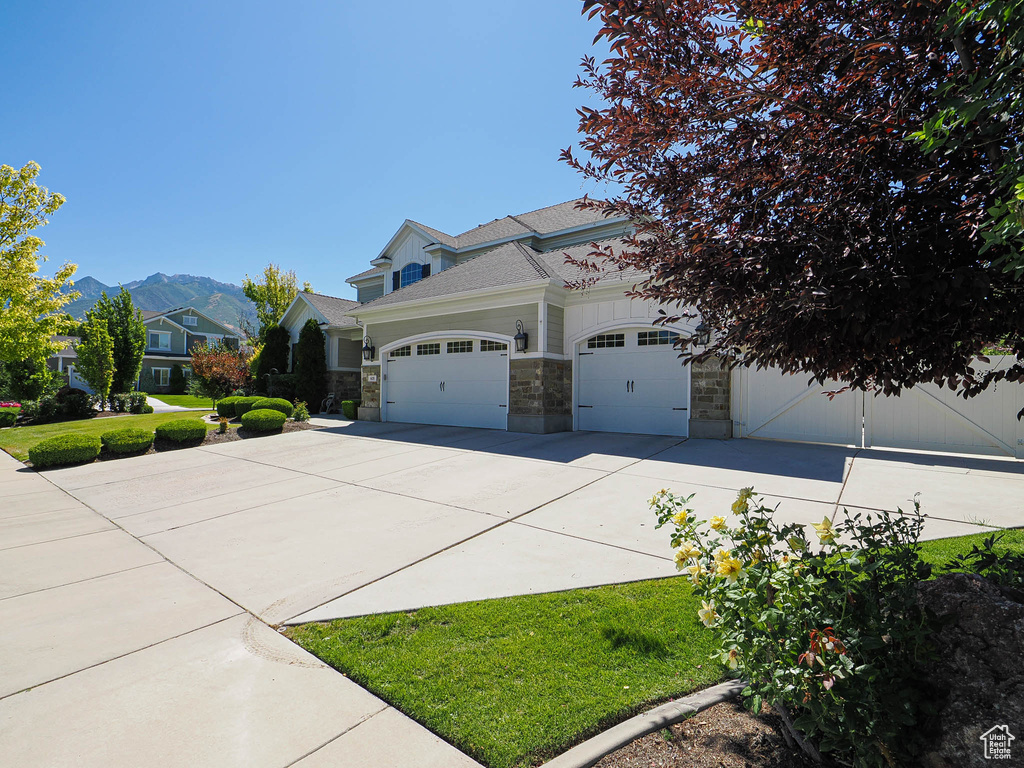 View of front of property with stone siding, concrete driveway, an attached garage, a mountain view, and a shingled roof