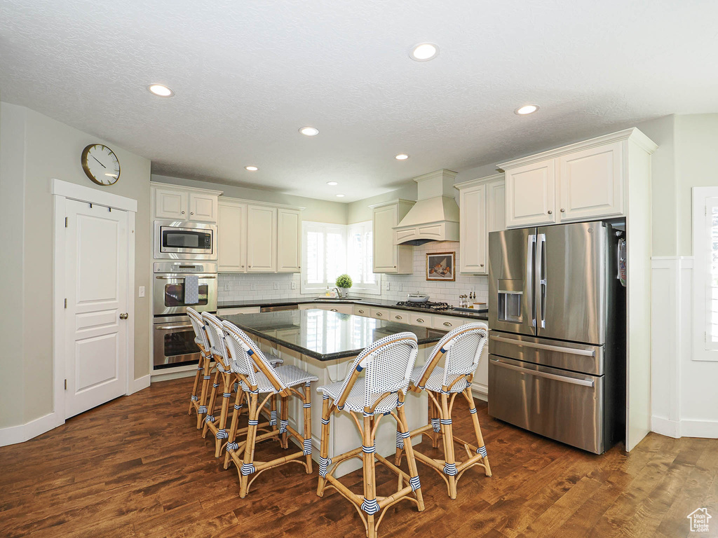 Kitchen featuring appliances with stainless steel finishes, custom exhaust hood, a breakfast bar, a center island, and backsplash