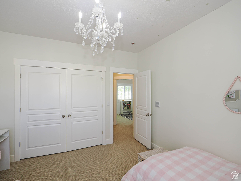 Bedroom with light colored carpet, a chandelier, and a closet
