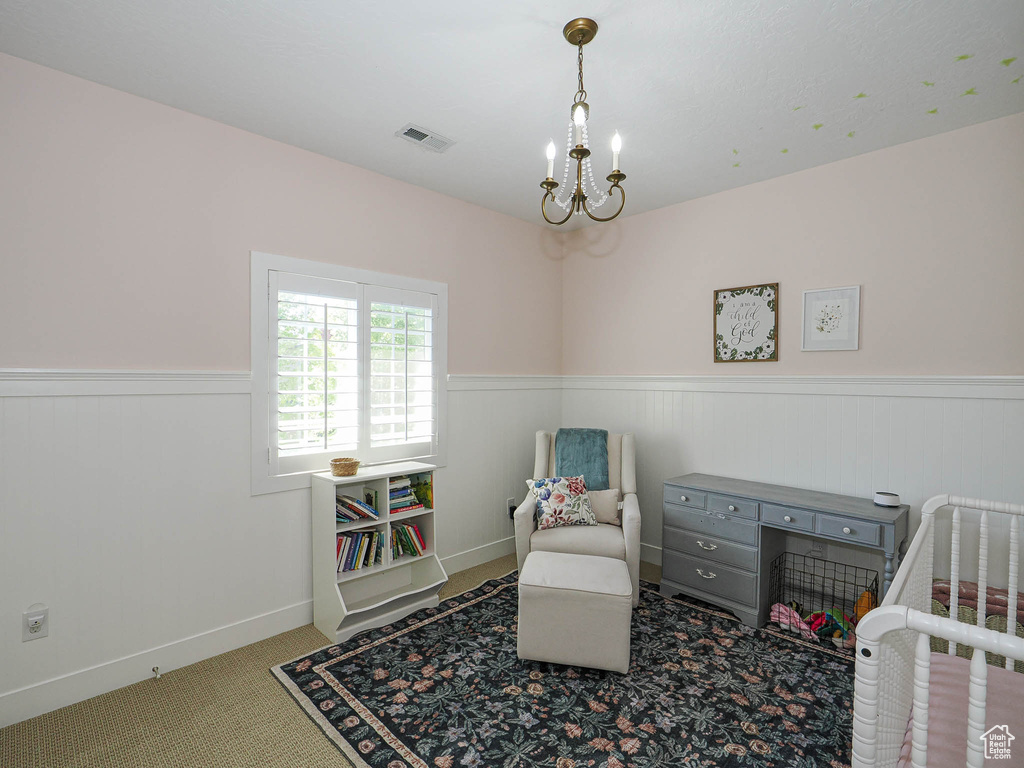 Bedroom featuring a wainscoted wall, a chandelier, a nursery area, and carpet floors