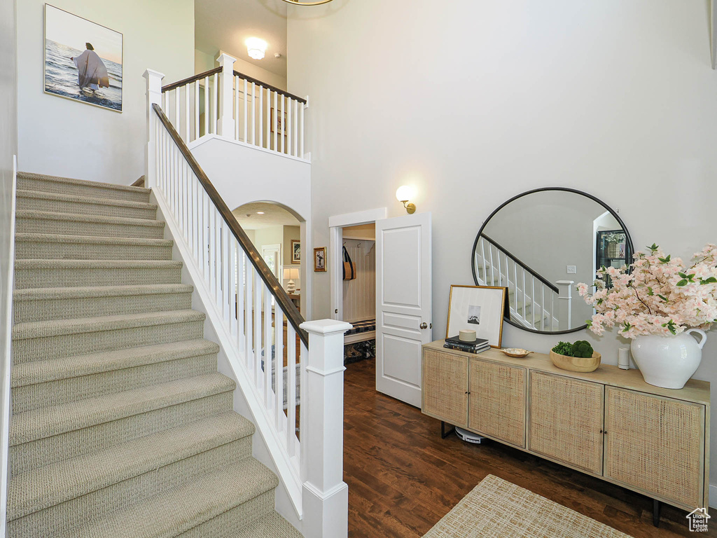 Staircase with wood finished floors, arched walkways, and a high ceiling
