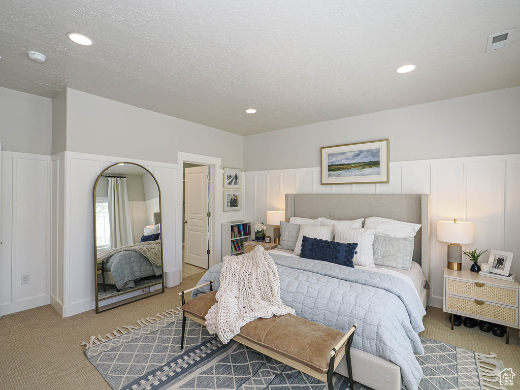 Bedroom with light carpet, a decorative wall, a textured ceiling, and recessed lighting