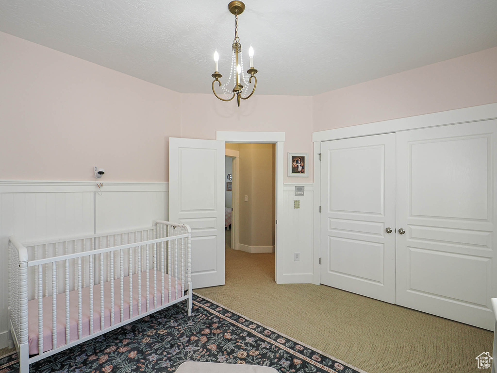 Carpeted bedroom featuring a chandelier, a wainscoted wall, a closet, and a crib