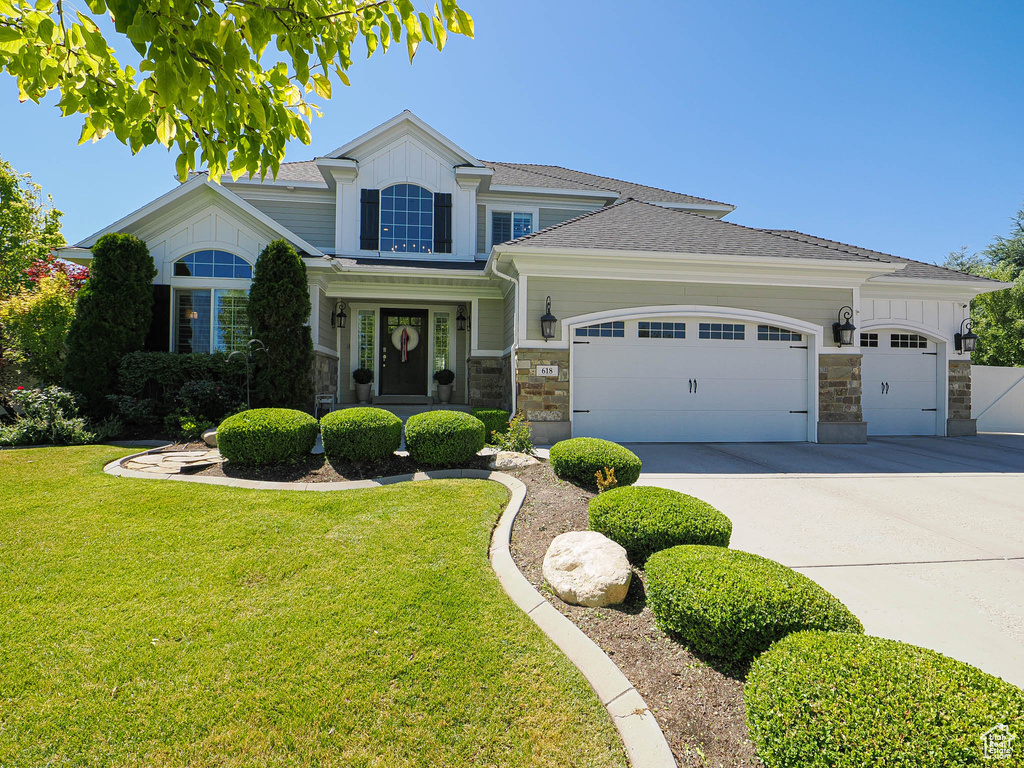 View of front of property with an attached garage, a front lawn, stone siding, concrete driveway, and board and batten siding