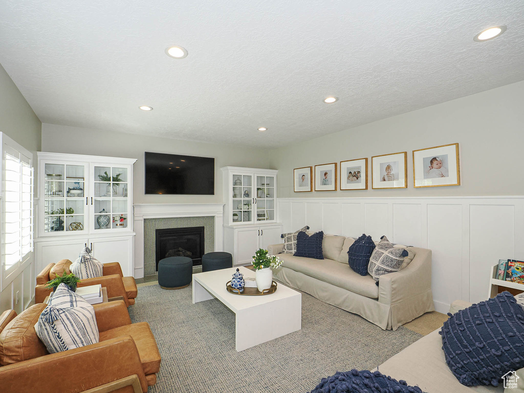 Living area featuring recessed lighting, wainscoting, a fireplace with flush hearth, a decorative wall, and a textured ceiling