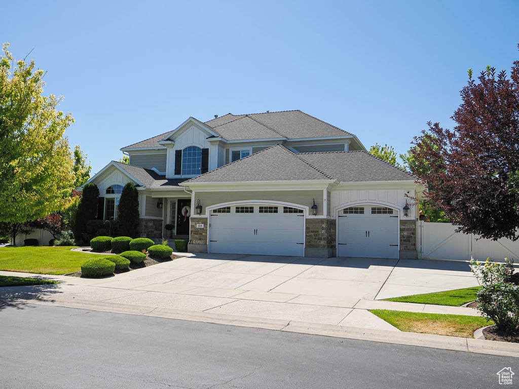 Craftsman house with an attached garage, stone siding, driveway, a shingled roof, and board and batten siding