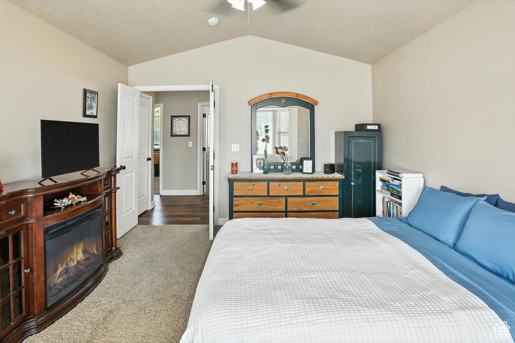 Bedroom with vaulted ceiling, carpet floors, a glass covered fireplace, and a ceiling fan