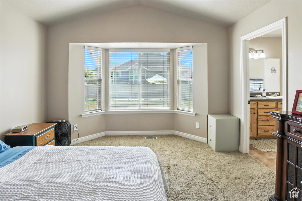 Bedroom with light colored carpet, lofted ceiling, and connected bathroom