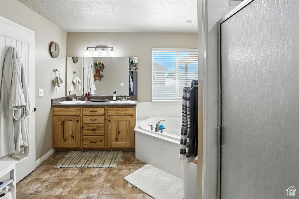 Bathroom with a bath, double vanity, a textured ceiling, and an enclosed shower