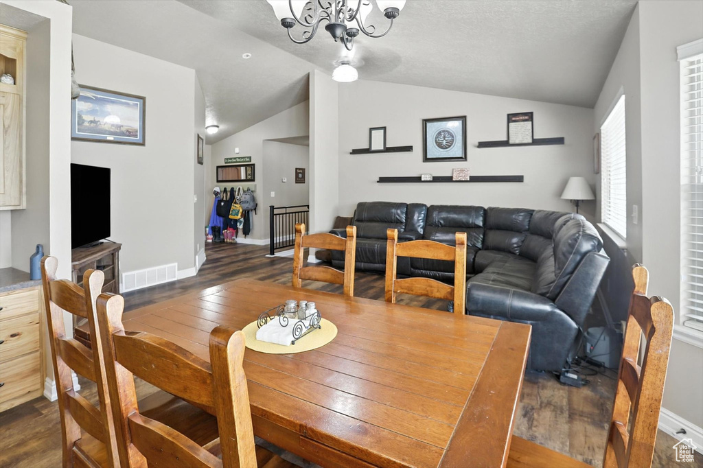 Dining space with dark wood finished floors, vaulted ceiling, and a chandelier