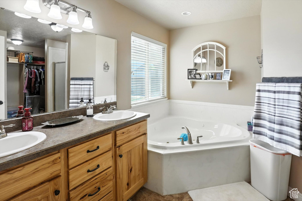Bathroom featuring double vanity, a jetted tub, and a spacious closet