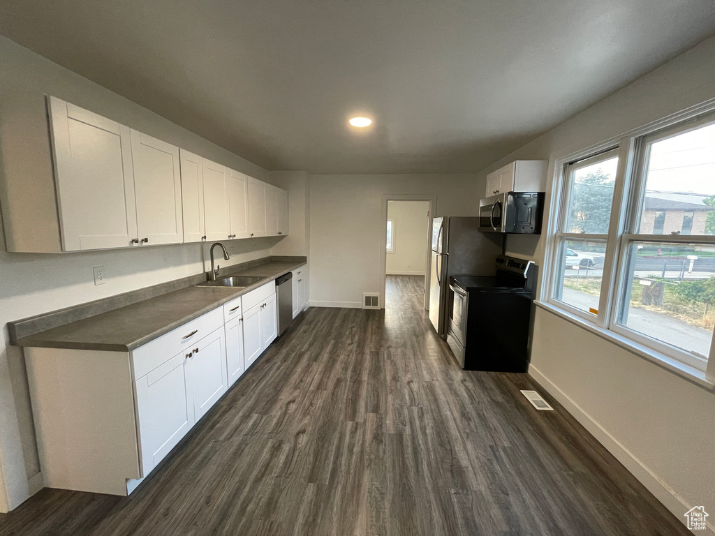 Kitchen with appliances with stainless steel finishes, dark wood-type flooring, white cabinets, dark countertops, and recessed lighting
