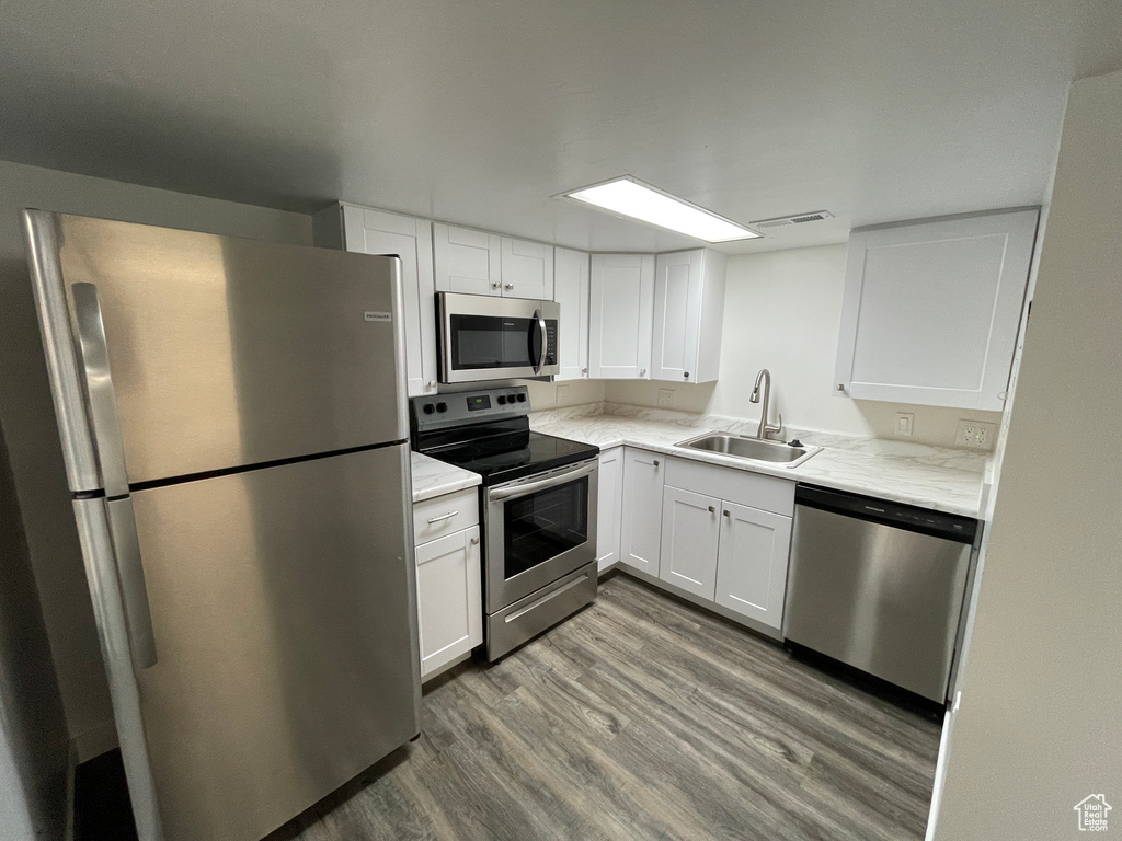 Kitchen featuring stainless steel appliances, wood finished floors, white cabinets, and light stone countertops