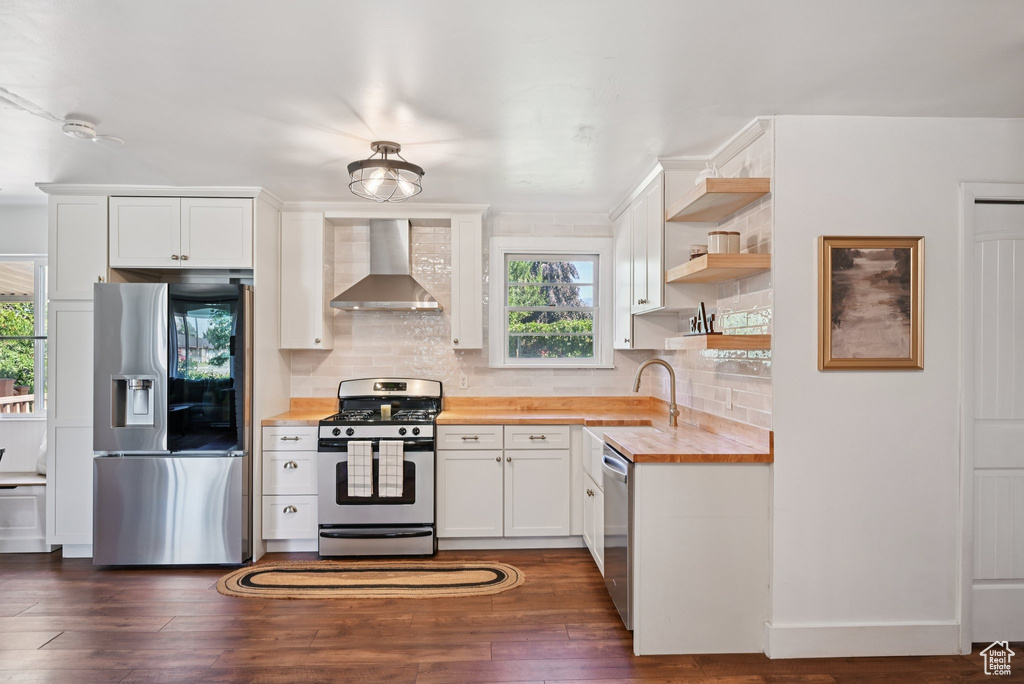 Kitchen with appliances with stainless steel finishes, wall chimney exhaust hood, butcher block counters, and healthy amount of natural light