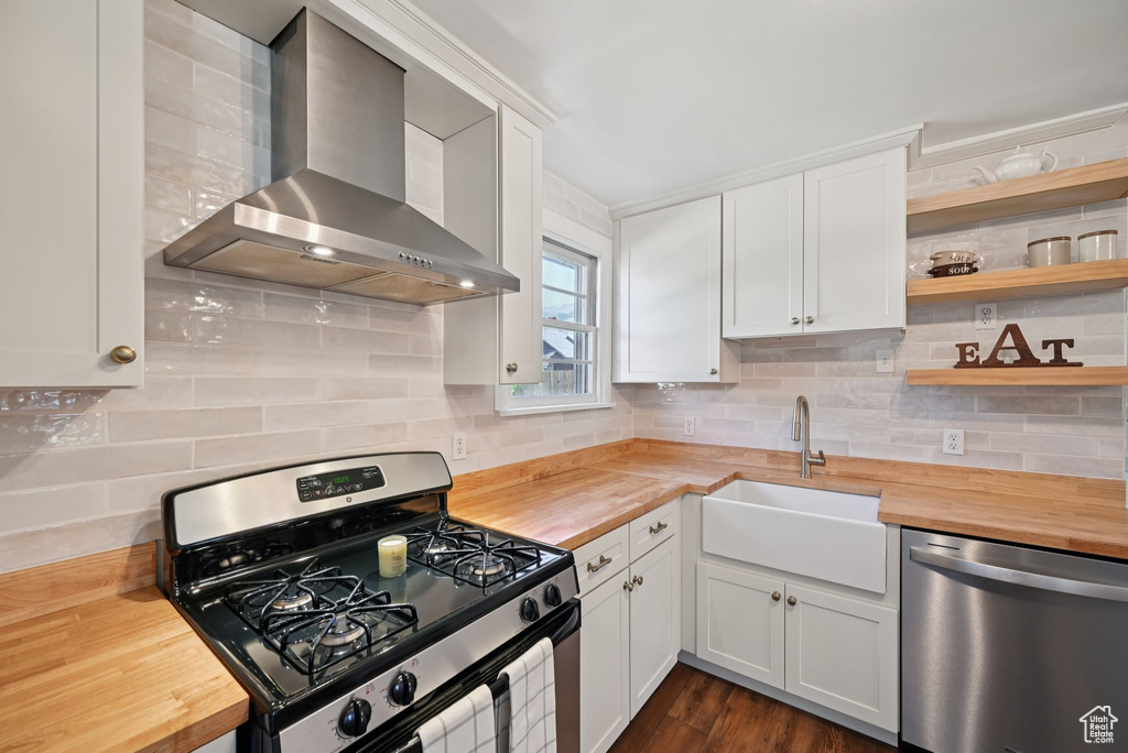 Kitchen featuring butcher block countertops, appliances with stainless steel finishes, wall chimney exhaust hood, and tasteful backsplash