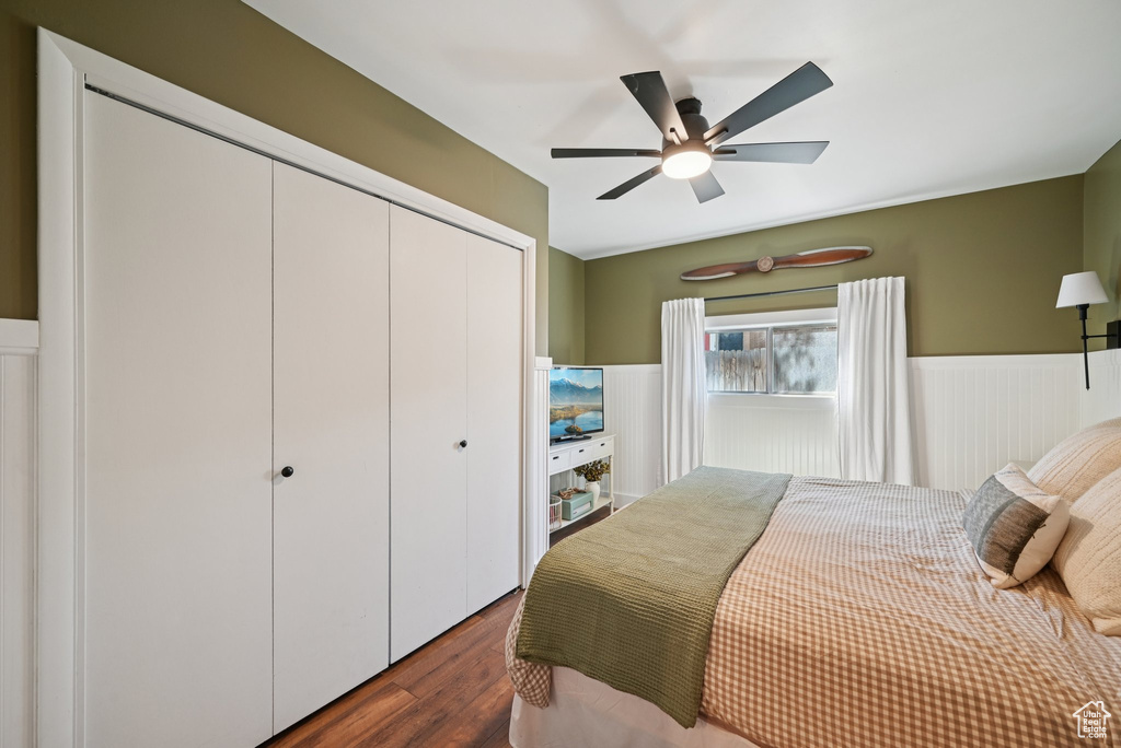 Bedroom with a wainscoted wall, a closet, dark wood finished floors, and a ceiling fan