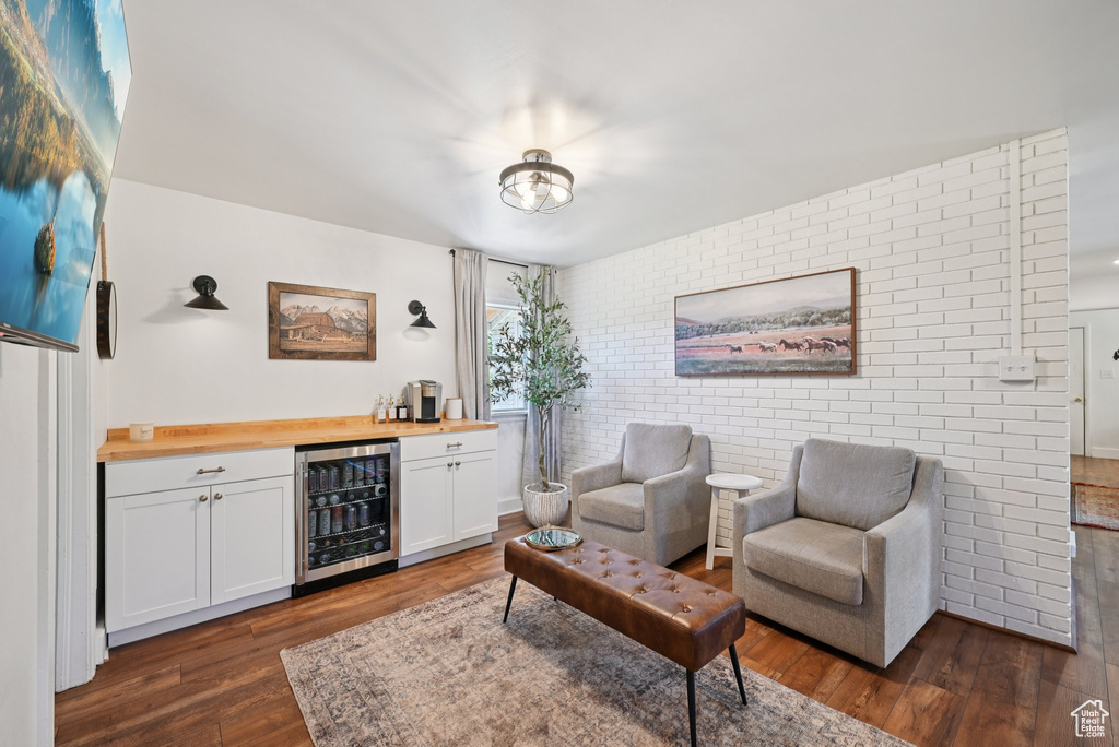 Living area featuring beverage cooler, a dry bar, dark wood finished floors, and brick wall